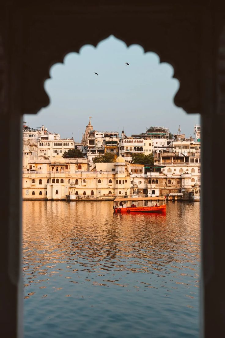 Cityscape with buildings reflected in water, viewed through an archway.
