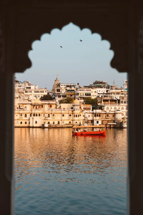 Cityscape with buildings reflected in water, viewed through an archway.