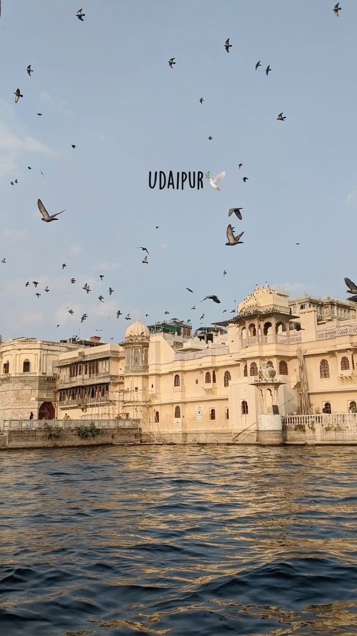 Historic building with birds flying over a body of water, Udaipur text overlay