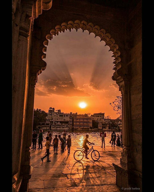 Sunset over a cityscape through an archway with people and a bicycle.