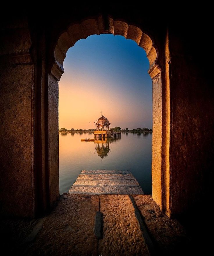 Archway leading to a serene lake with a small pavilion at sunset.