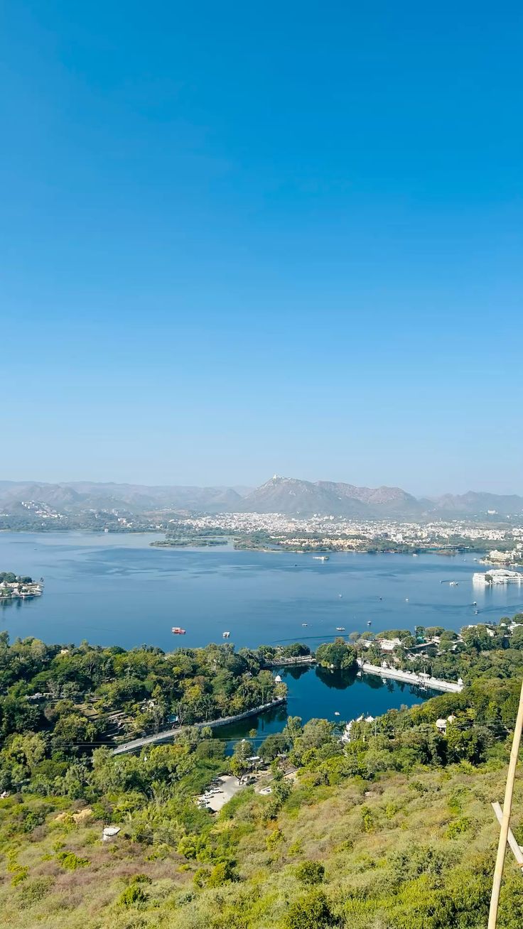Scenic view of a lake with greenery and distant buildings under a clear blue sky.