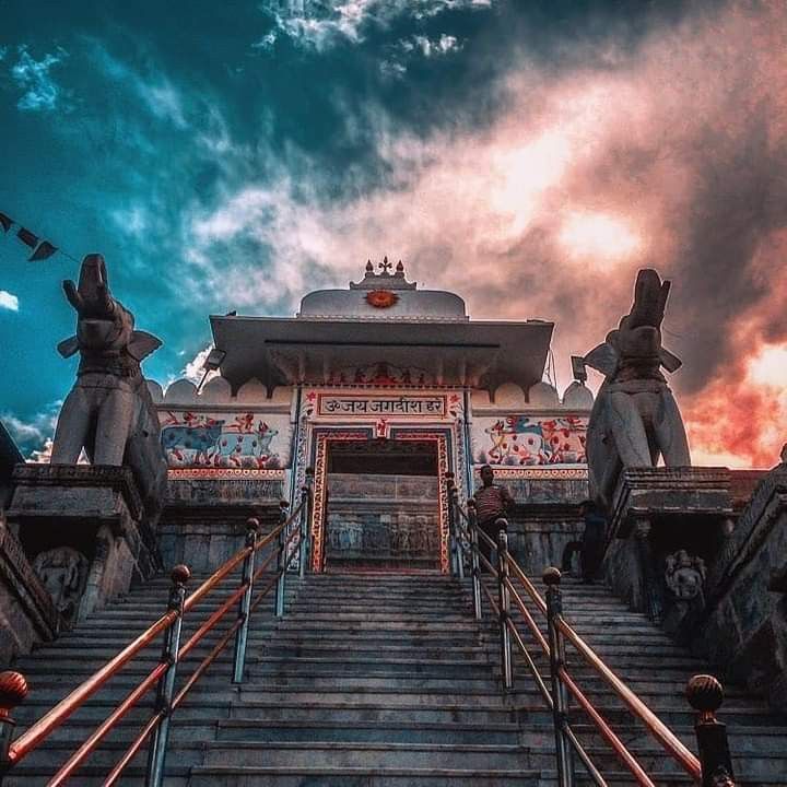 Stairway leading up to a temple with statues on either side against a dramatic sky.