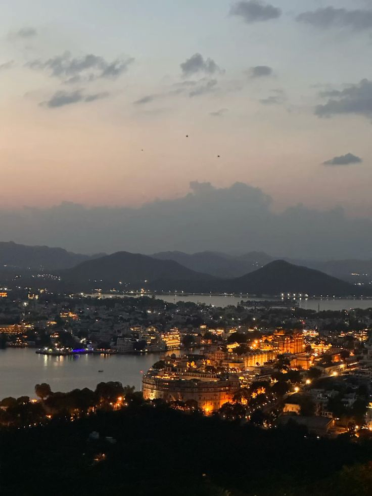 Cityscape at dusk with illuminated buildings and mountains in the background